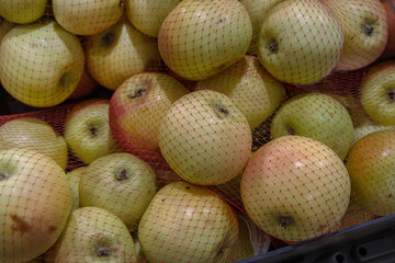 Fresh green and red apples in red plastic shopping net. Fruits arranged in the grocery store on the counter. Apples pile on food market rack. Variety of fruits sold in the food shop. Close-up.