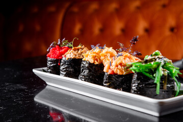 Five gourmet sushi rolls with various toppings, served on a white plate against a dark, elegant background. Perfect for upscale dining