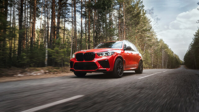 Seattle, Washington, USA April 7, 2024: The red updated BMW X5 m Competition car moves along the highway in the forest. Luxury SUV from a famous German brand. front view