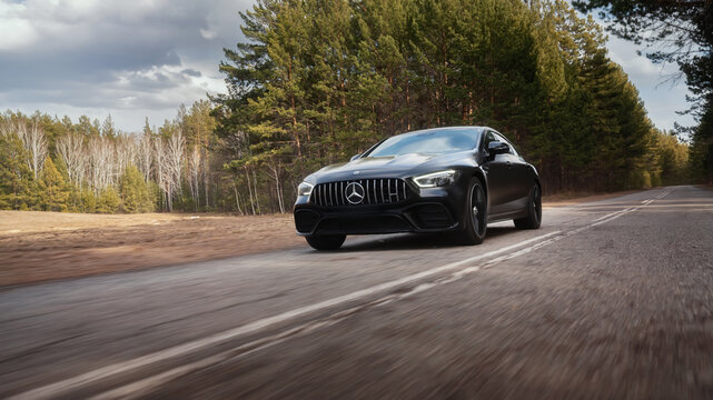 Seattle, Washington, USA April 7, 2024: Mercedes-Benz AMG GT 43 matte black, moving along a highway in the forest. A luxury car from a famous German brand. foreground
