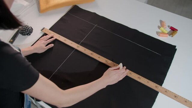 A woman's hands is measuring a piece of fabric with a ruler