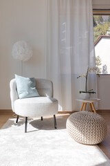 Detail of a living room corner with a small armchair with a coffee table and a pouf resting on the carpet. - 782011294