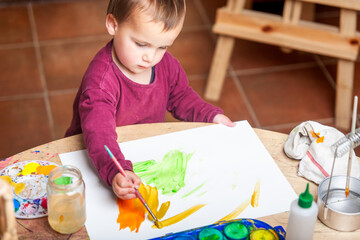 Little boy painting his white canvas with acrylic paints.