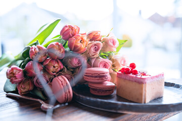 Beautiful pink bouquet of flowers with sweet delicacies. Heart shape, sweet pastries with pink roses and tulips on a wooden table. Background for mother's day and weddings.
