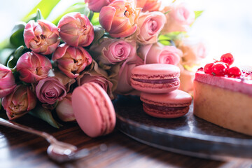 Beautiful pink bouquet of flowers with sweet delicacies. Sweet pastries with pink roses and tulips on a wooden table. Background for mother's day and weddings. Close-up. - obrazy, fototapety, plakaty
