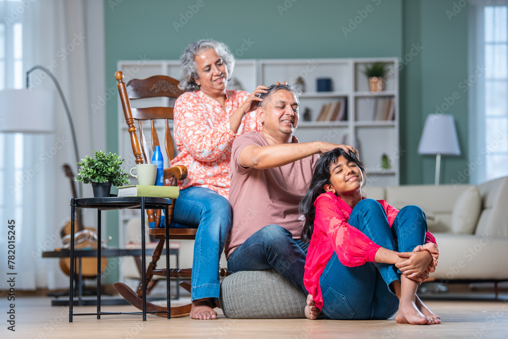 Wall mural indian asian grand child receiving head massage from father and mother in living room