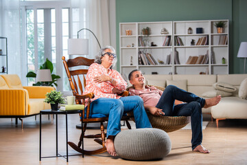 Selective focus of cheerful senior Indian couple watching tv on couch in living room