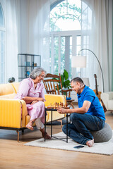 Mature Indian couple enjoying while playing chess board game together at home