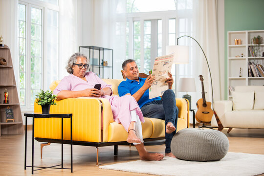 Indian asian mid age man reading newspaper, his wife using phone.
