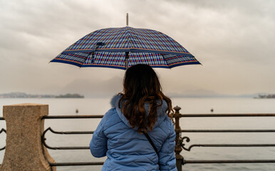Attractive middle-aged woman sitting from behind in the rain with an umbrella in front of Lake Maggiore