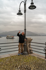 Attractive middle-aged man using mobile phone standing near a street lamp on the lakeside in Stresa