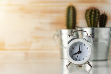 White alarm clock with cactus in pot on wooden desk. Minimal time concept.