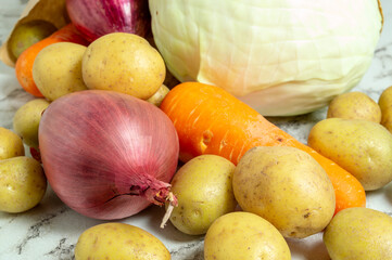 A bunch of vegetables including potatoes, onions, and carrots are spread out on a counter. Concept of abundance and freshness, as the vegetables are piled high and appear to be in good condition