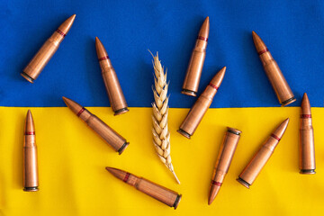 Wheat grains with Ukrainian flag on wooden background with metal bullet shells.