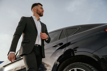 Businessman in suit is near his black car outdoors