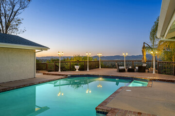 Fototapeta premium Outdoor pool at sunset with illuminated patio furniture and lights in Encino, CA