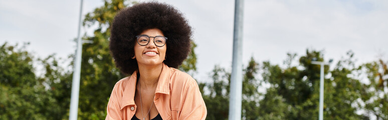A stylish young African American woman with curly hair wearing glasses and a pink shirt...