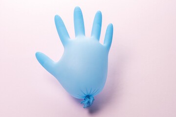 Blue latex medical glove on pastel pink backdrop. Minimal Coronavirus outbreak. Panic concept.