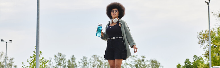 Young African American woman with a curly afro hair riding a skateboard at a skate park.