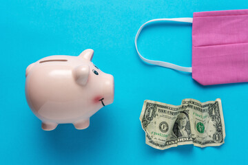 Piggy bank with a medical face mask and crumpled dollar bancnote. Minimal Coronavirus outbreak....
