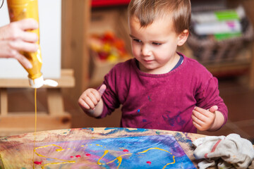 Toddler watches as gold paint is poured over his canvas.