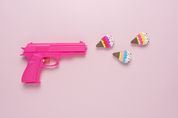 Holiday concept with Pink handgun on pink pastel background with ice cream decor. Minimal creative concept.