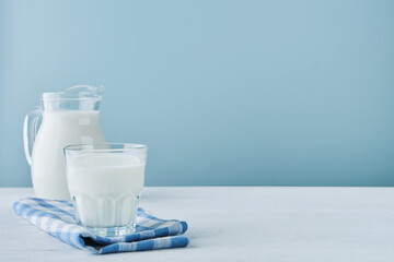 Milk in jug and glass on wooden table and blue background. Concept of farm dairy products, milk...