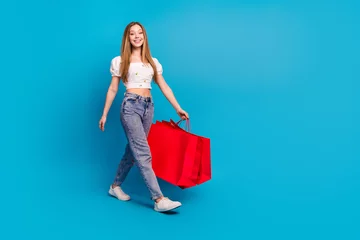 Gordijnen Full length portrait of lovely girl shop bags walk empty space wear top isolated on blue color background © deagreez