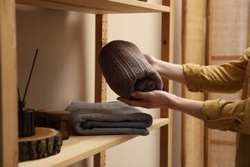 Woman putting rolled towel onto shelf indoors, closeup