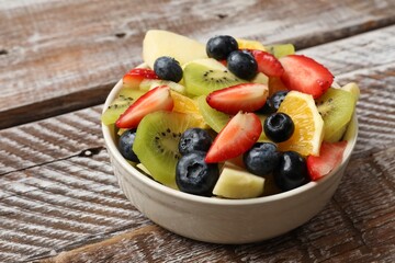 Tasty fruit salad in bowl on wooden table, closeup