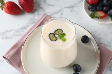 Tasty yogurt in glass and berries on white marble table