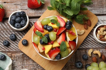 Tasty fruit salad in bowl and ingredients on wooden table, flat lay
