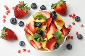 Tasty fruit salad in bowl and ingredients on white table, flat lay