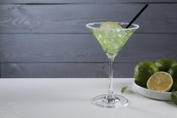 Delicious Margarita cocktail with ice cubes in glass and lime on white table, space for text