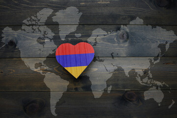 wooden heart with national flag of armenia near world map on the wooden background.