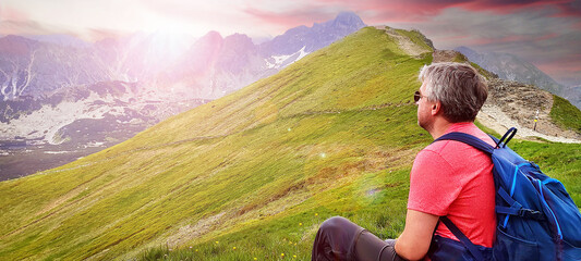 Active senior elderly man with backpack enjoying sunset on mountain. Tourist traveler looking to...