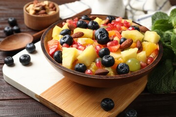 Delicious fruit salad in bowl, berries, nuts and fresh mint on wooden table