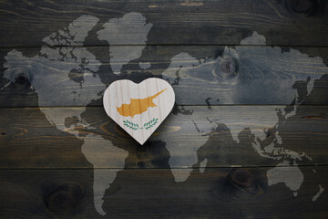 wooden heart with national flag of cyprus near world map on the wooden background.