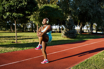An African American woman in sportswear stands with arms crossed on a track, exuding confidence and...