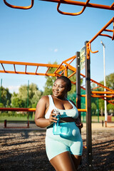 An African American woman in a blue and white sportswear runs in front of a playground, showing body positivity and confidence.