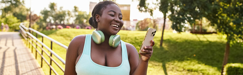 An African American woman joyfully listens to music on her cell phone while wearing headphones outdoors.