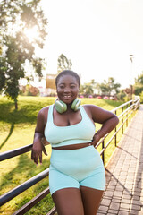 An African American woman with headphones, wearing a blue top and shorts, confidently poses for a picture outdoors.