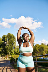 An African American woman enthusiastically exercises outdoors in a blue sports bra and matching...