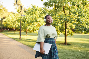 A plus size African American woman in casual attire walks confidently on a park sidewalk in summer.
