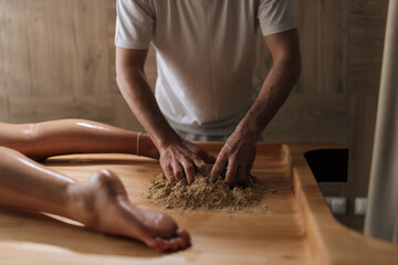 Cropped shot of unrecognizable massage practitioner male mixing heated sand on massage table for...