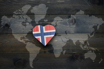 wooden heart with national flag of norway near world map on the wooden background.