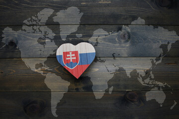 wooden heart with national flag of slovakia near world map on the wooden background.