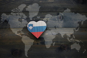 wooden heart with national flag of slovenia near world map on the wooden background.
