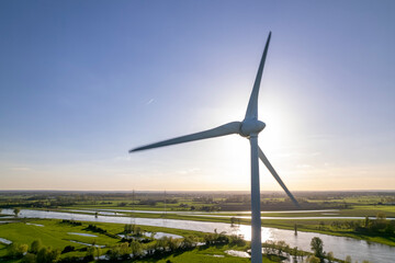 Sun behind wind turbine in The Netherlands part of Dutch 
sustainable industry along river IJssel and Twentekanaal waterway picturesque landscape. Aerial circular economy concept
