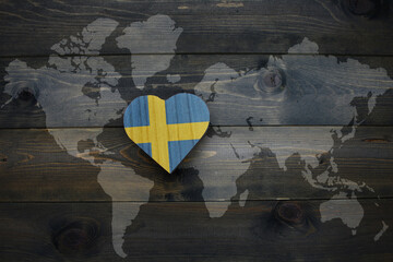 wooden heart with national flag of sweden near world map on the wooden background.